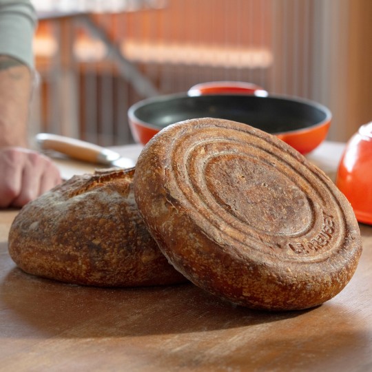 two loaves of freshly baked bread in front of a Le Creuset bread oven