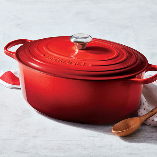 red oval dutch oven on counter with a wooden spoon