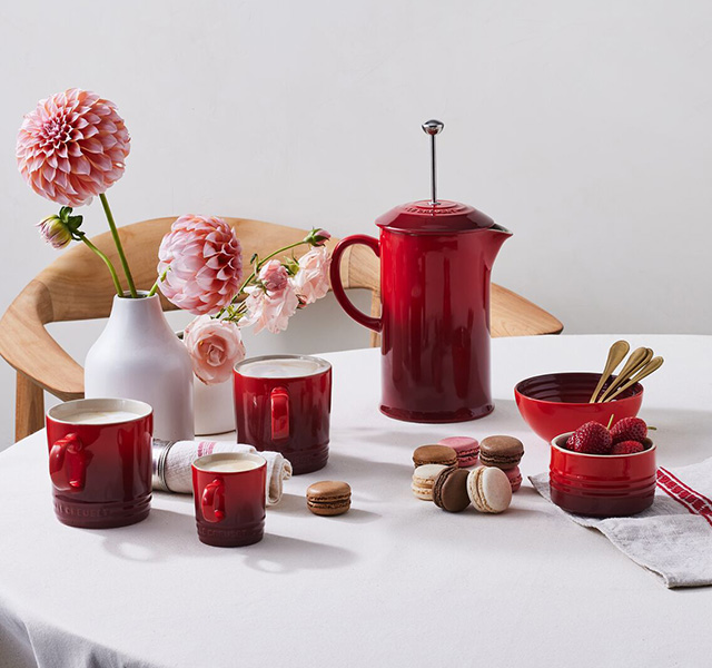 Mesa posta, com três tamanos de canecas vermelhas, prensa francesa e acompanhamentos para o café
