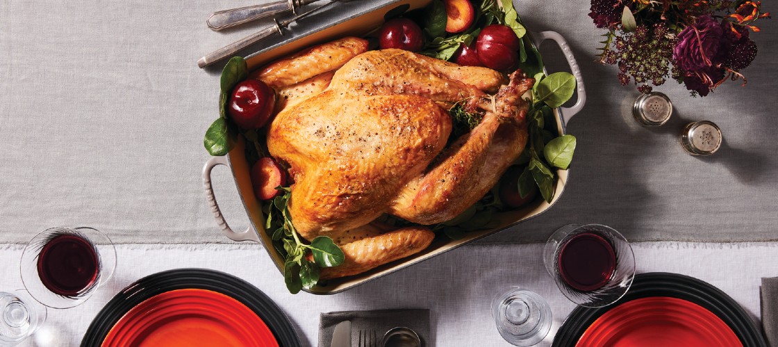roasted turkey in a cast iron roaster on a table set for Thanksgiving dinner