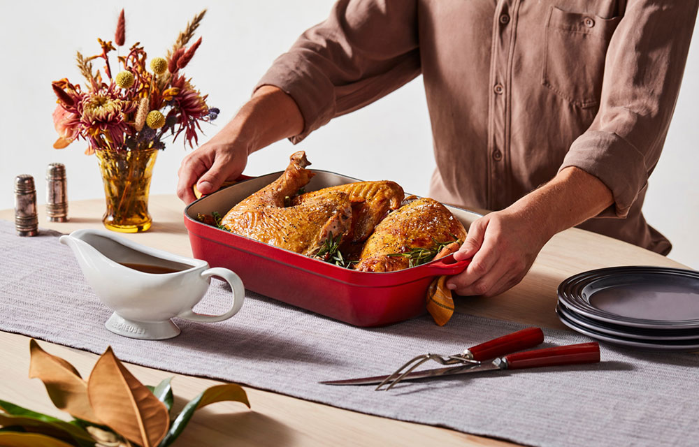 person placing turkey in cast iron roaster on a table